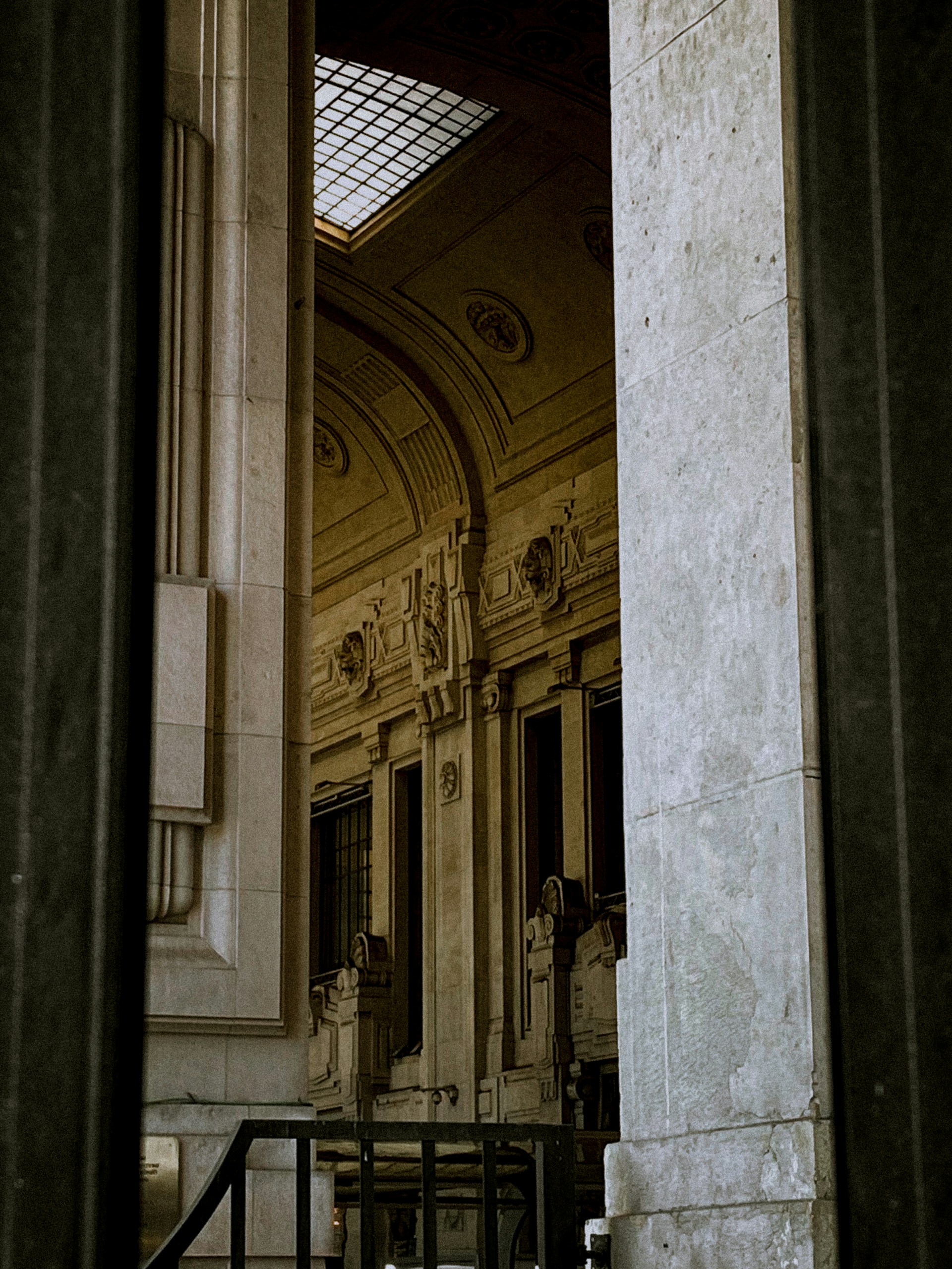 Elegant architectural details with intricate carvings and large windows are partially visible, framed by tall stone pillars. A skylight lets in natural light, highlighting the craftsmanship of the interior space.