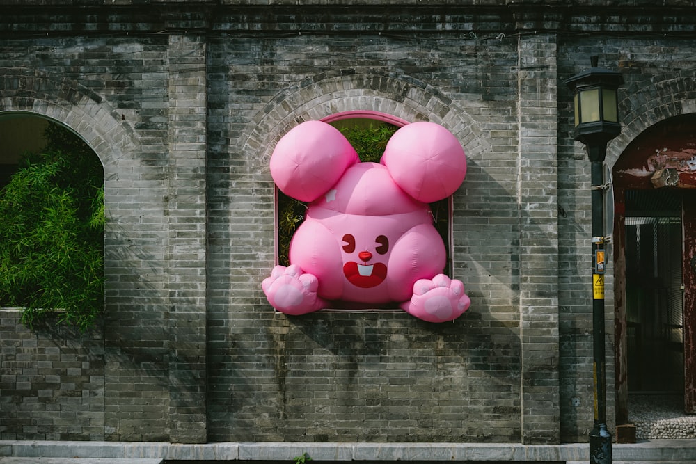 a pink balloon shaped like a bunny hanging from a brick wall