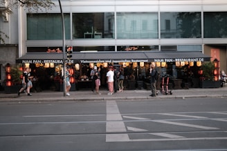 A group of people stand outside a Vietnamese and Japanese restaurant named Nam Pan. The restaurant features traditional lanterns and decorative elements. Several pedestrians are passing by on the sidewalk.