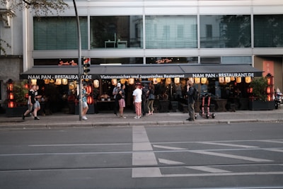 A group of people stand outside a Vietnamese and Japanese restaurant named Nam Pan. The restaurant features traditional lanterns and decorative elements. Several pedestrians are passing by on the sidewalk.