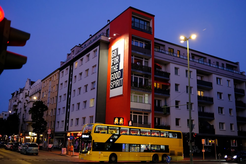 a yellow double decker bus driving past a tall building