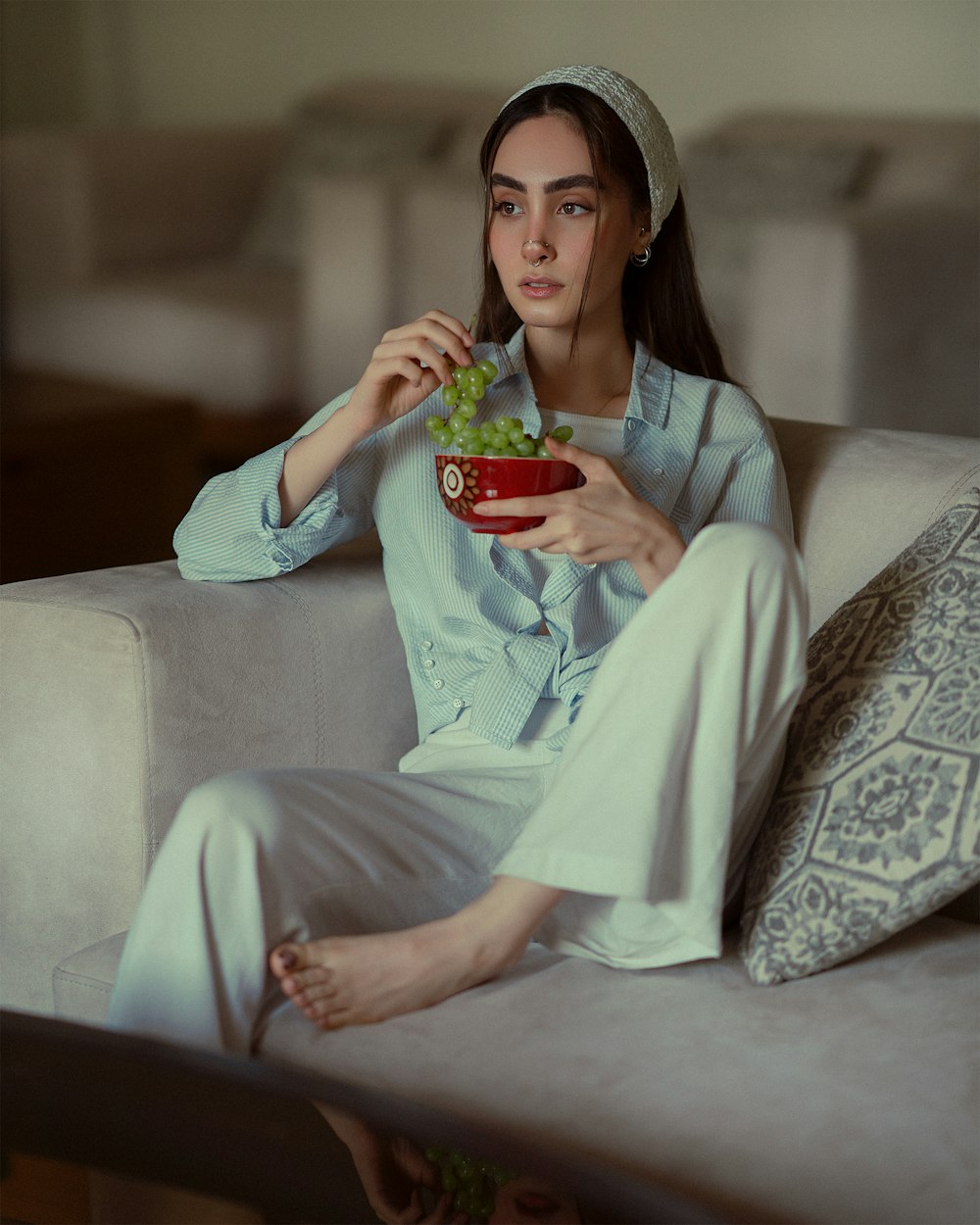 a woman sitting on a couch holding a bowl of grapes