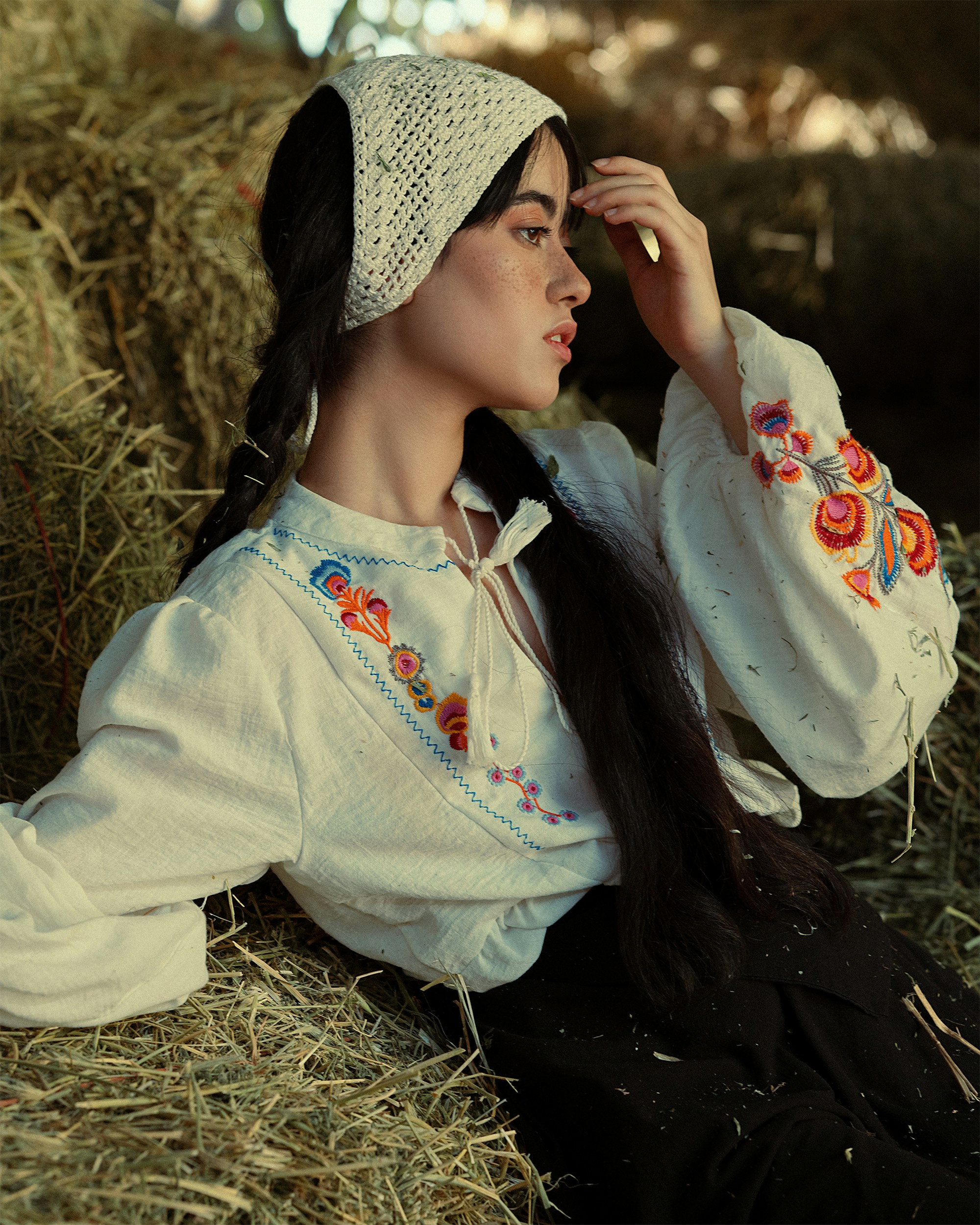 a woman with long hair sitting on a pile of hay