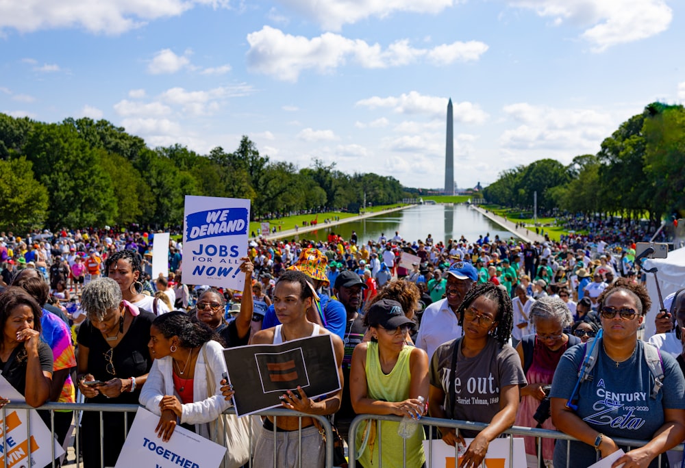 a crowd of people holding signs in front of a fountain