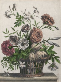 A woven basket is filled with a variety of flowers in full bloom. The flowers exhibit an array of colors, predominantly in shades of pink and white, with lush green leaves extending from the stems. The arrangement is set against a plain background, resting on a flat surface, and showcases a harmonious blend of colors and textures.