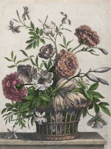 A woven basket is filled with a variety of flowers in full bloom. The flowers exhibit an array of colors, predominantly in shades of pink and white, with lush green leaves extending from the stems. The arrangement is set against a plain background, resting on a flat surface, and showcases a harmonious blend of colors and textures.