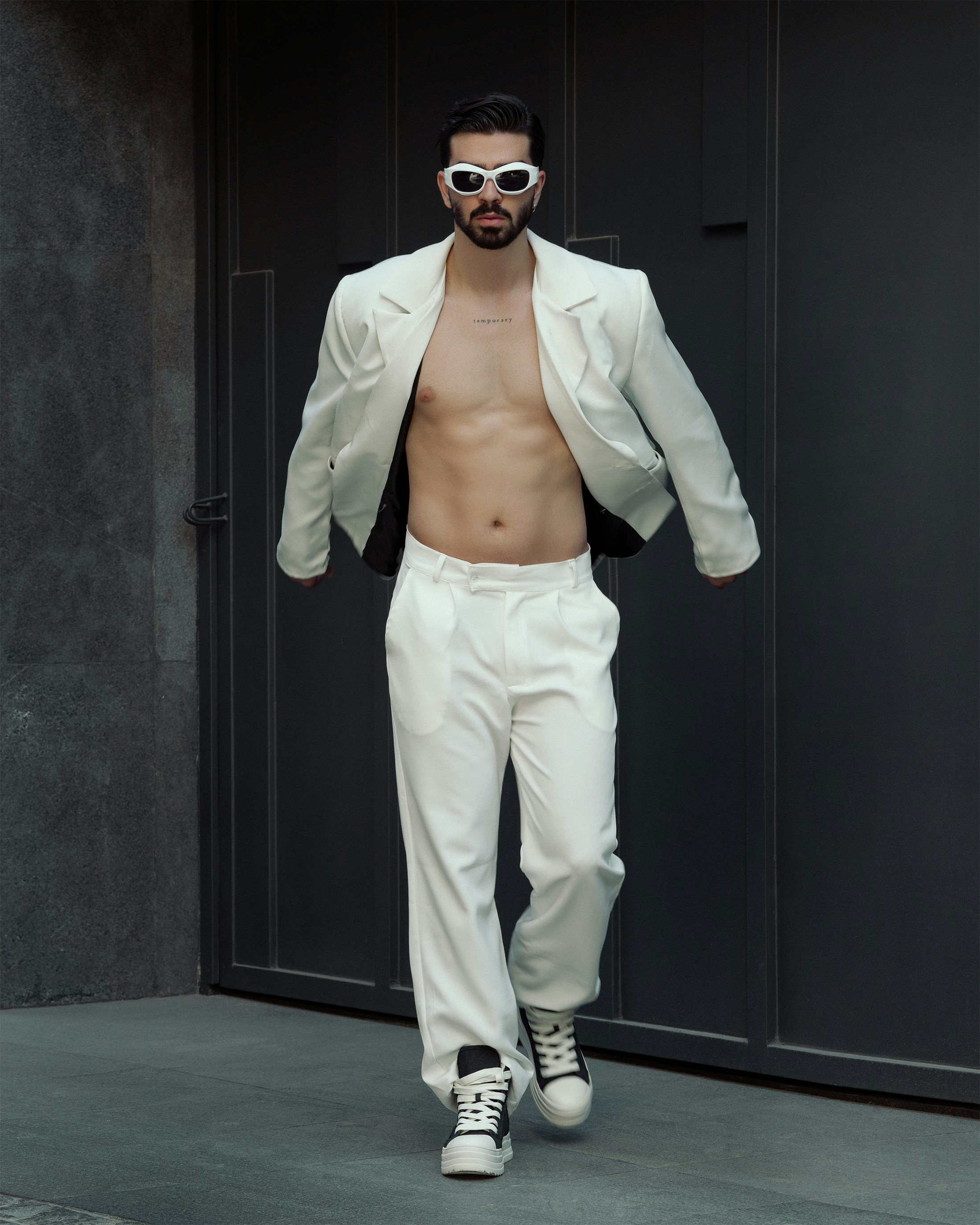 a man in a white suit and sunglasses walking down a runway