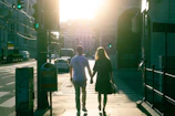 Natural light portrait of a couple walking hand-in-hand on a sunlit street.