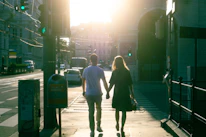 A couple holding hands, walking together through a sunlit park.
