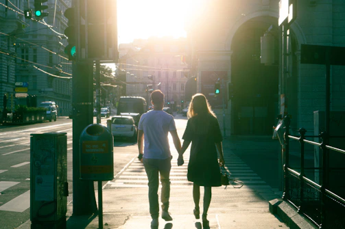 Natural light portrait of a couple walking hand-in-hand on a sunlit street.