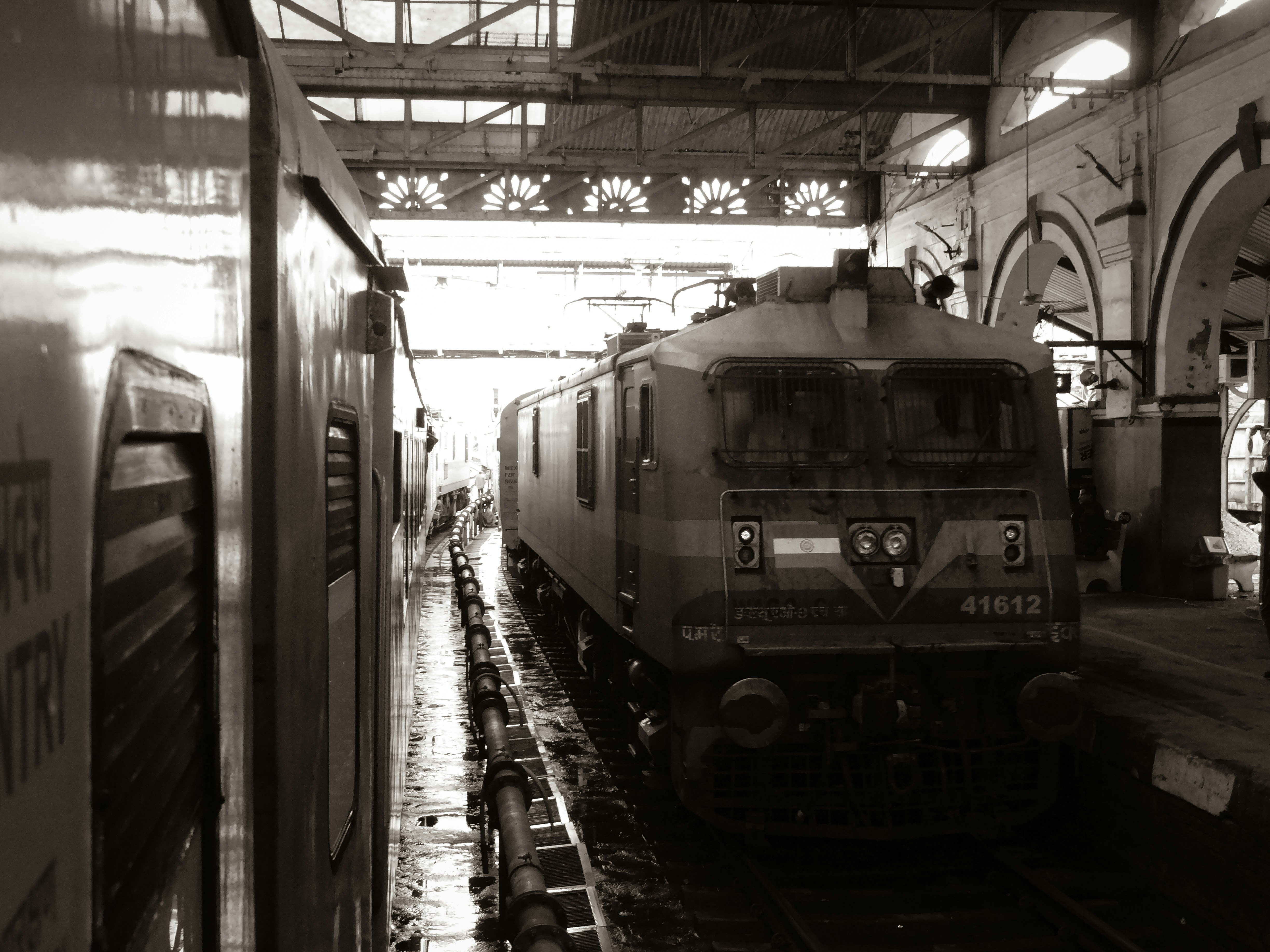 a black and white photo of a train in a train station, "Busy station scenes" Dehradun Shatabdi with a Ghaziabad WAP7 prepares for departures, as it greets the Nauchandi Express arriving from Prayagraj behind a Itarsi WA9HC.