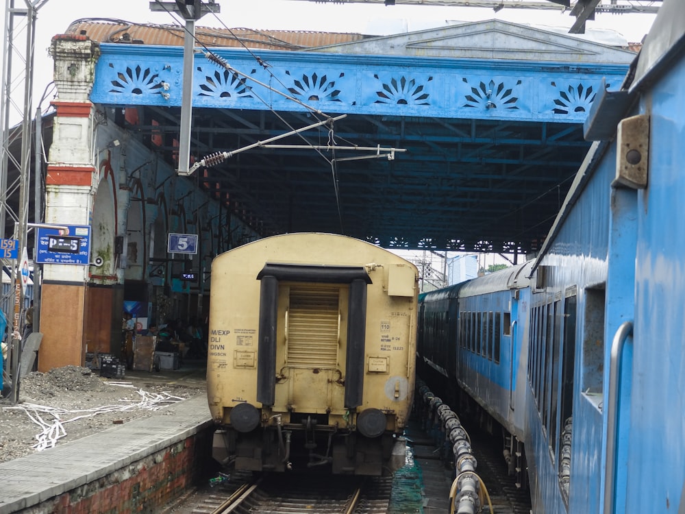 a yellow train traveling under a blue bridge