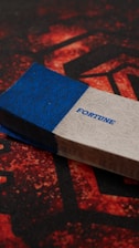 A stack of cards is placed on a surface featuring a red and black geometric pattern. The top card has a blue and white design with the word 'FORTUNE' written in blue. The card stack appears slightly worn with textured edges.