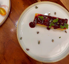 Close-up of a rich, spiced dessert topped with fresh fruit, set against deep red and earthy-toned textiles.