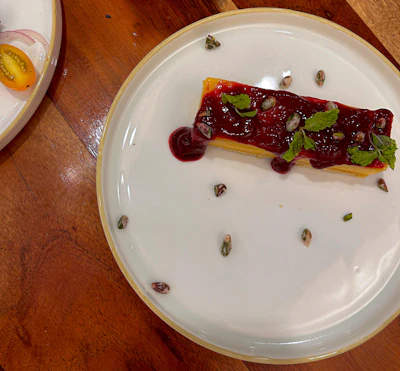 Close-up of a rich, spiced dessert topped with fresh fruit, set against deep red and earthy-toned textiles.