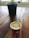 A wooden table with a small plant in a black pot in the background and a red coffee cup labeled '100% Recyclable' in the foreground. The coffee cup is filled with frothy coffee.