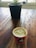 A wooden table with a small plant in a black pot in the background and a red coffee cup labeled '100% Recyclable' in the foreground. The coffee cup is filled with frothy coffee.