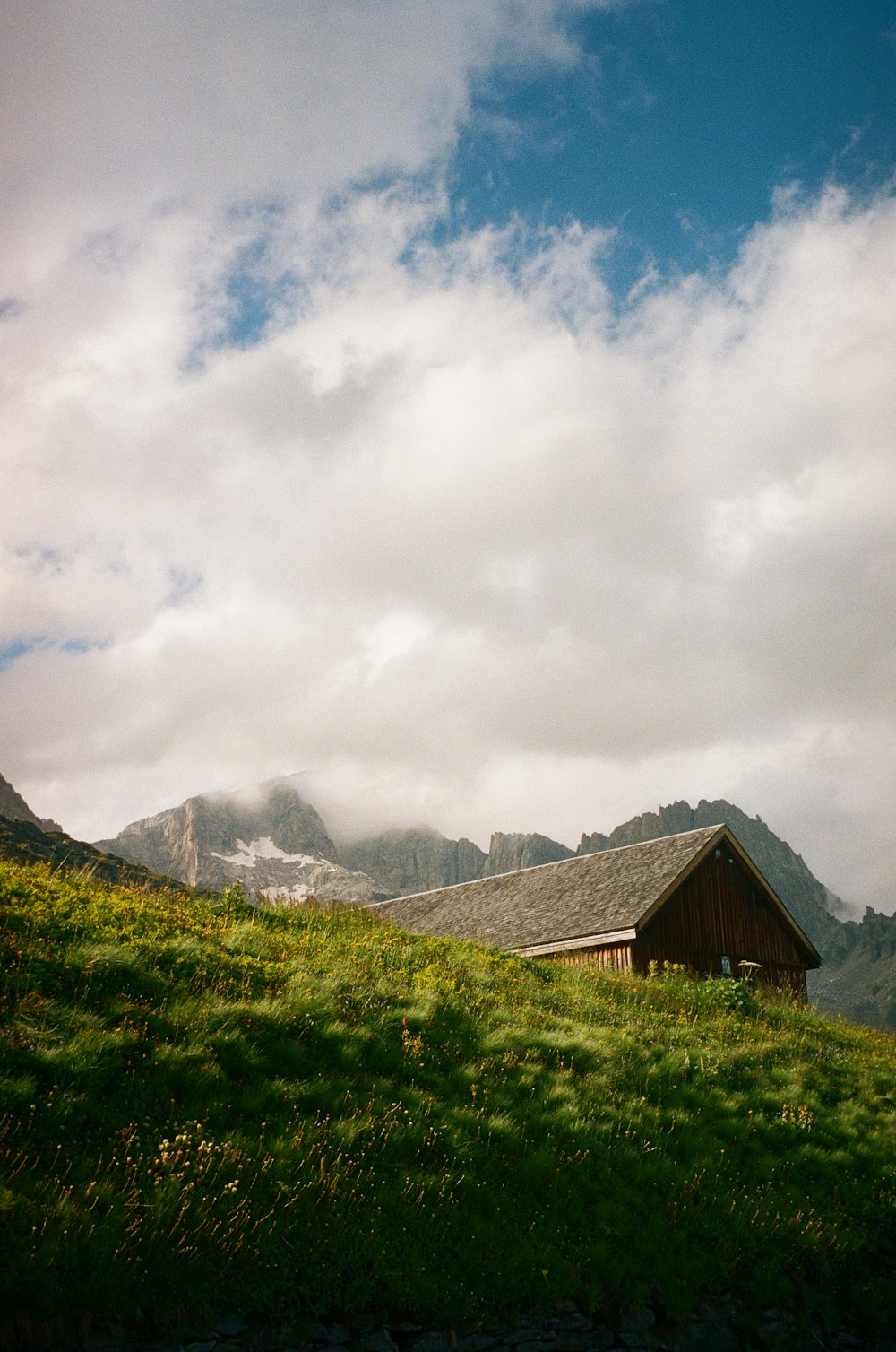 une maison sur une colline herbeuse avec des montagnes en arrière-plan