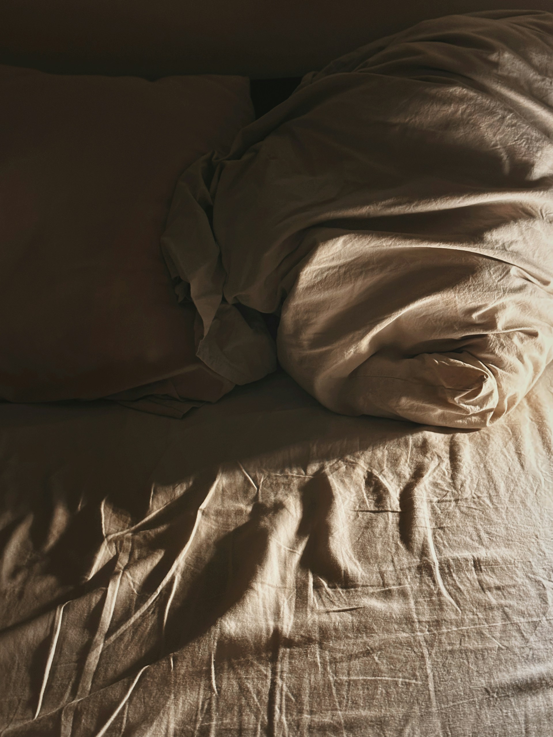 an unmade bed with a brown comforter and pillows