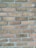 A close-up view of a brick wall composed of uniform rectangular bricks arranged in a horizontal pattern. The bricks are light brown and feature a rough texture, with grey mortar filling the gaps between them.