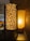 Two decorative lamps are placed side by side on a dark surface. The lamp on the left has a cylindrical shade with a leopard print design, standing on a wooden frame. To the right, another lamp with a bubble-textured shade emits a warm, yellowish light. Shadows and patterns are softly cast on the background wall.