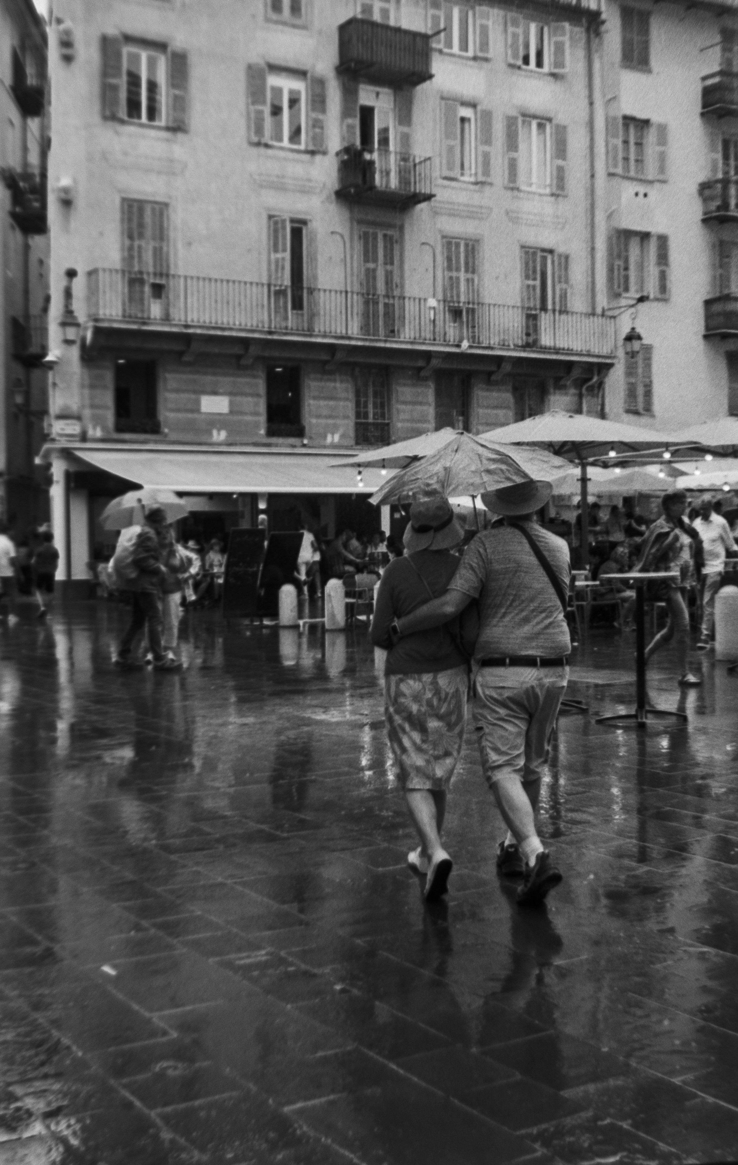 a black and white photo of two people walking in the rain