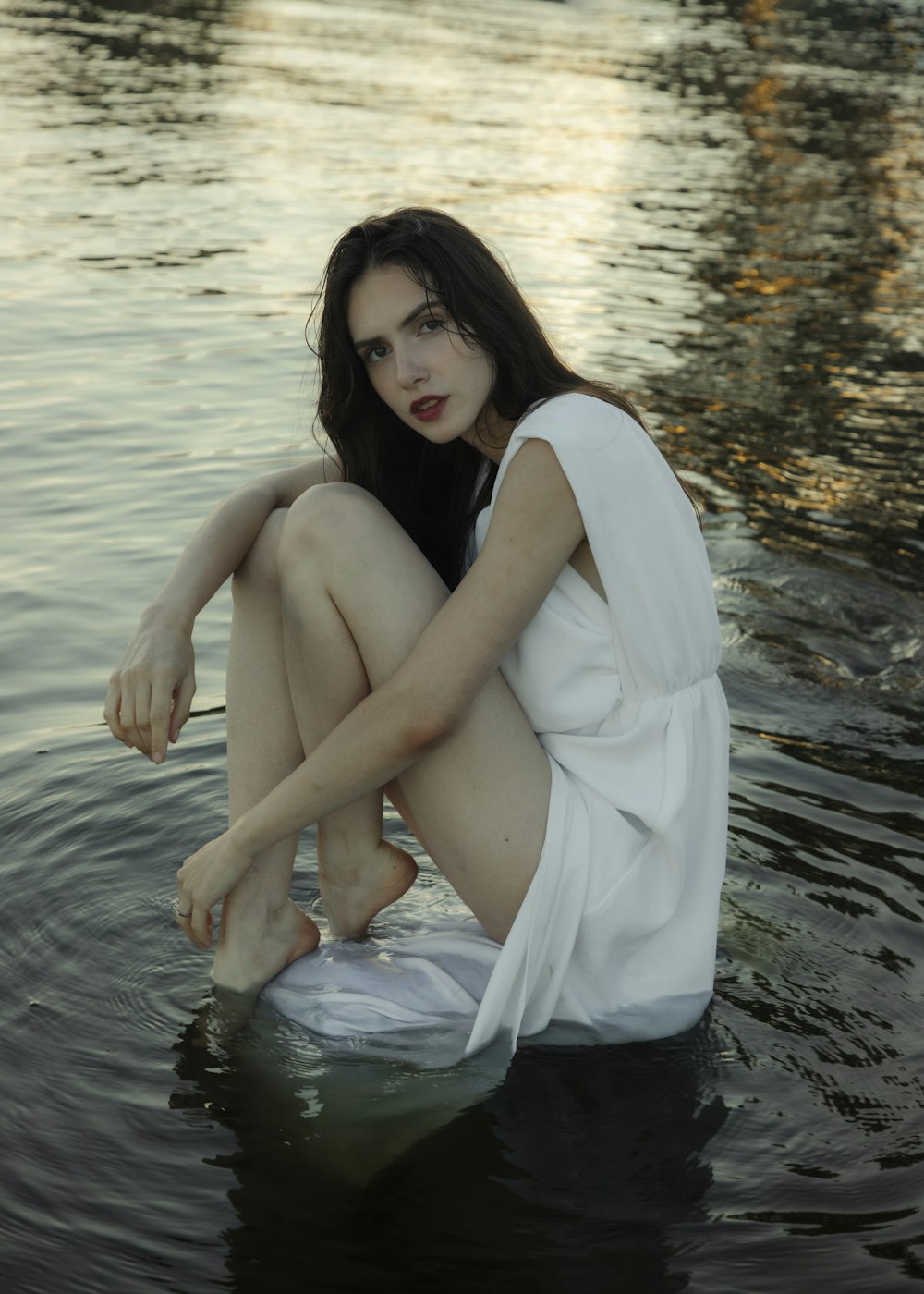 a woman is sitting on a rock in the water