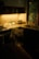 A warmly lit kitchen corner featuring a countertop with a potted plant, a toaster, and several soap dispensers near a stainless steel sink. The wooden cabinetry and appliances are partially illuminated by soft natural light coming through a window, creating an inviting and serene atmosphere.