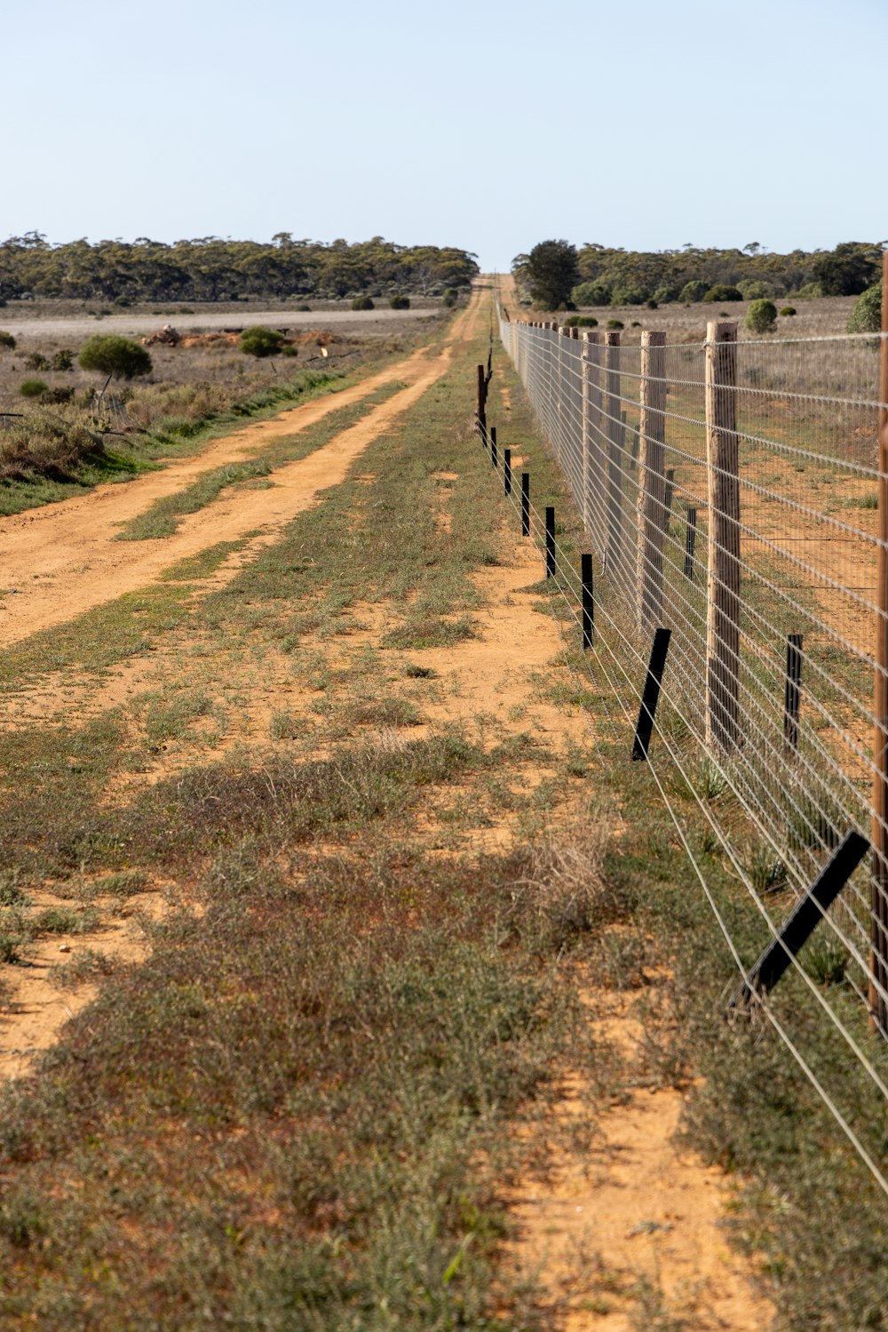 a dirt road with a wire fence on the side of it