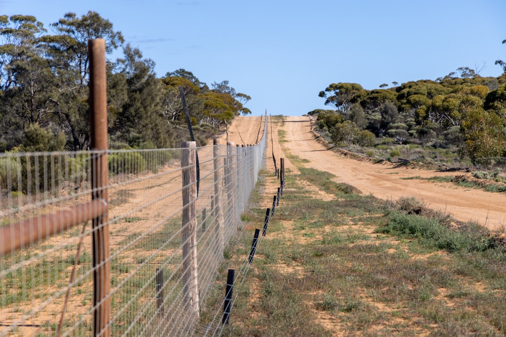 a dirt road next to a fence and a dirt road