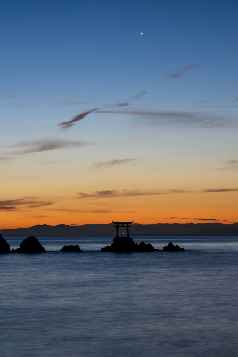 a sunset view of a body of water with rocks in the foreground