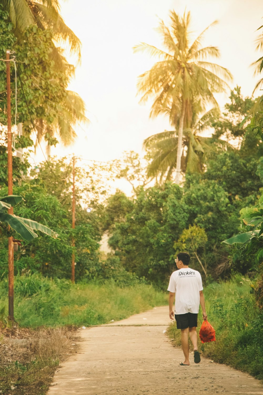 a man walking down a dirt road holding a red frisbee