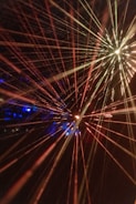 Bright, colorful laser beams radiate in various directions against a dark background, creating a dynamic and energetic composition. The beams converge towards the center and display a spectrum of colors including red, yellow, and hints of blue. The vibrant lights create a sense of movement and depth.