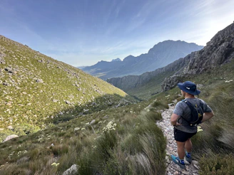 A smiling traveler standing on a scenic mountain trail in Georgia, surrounded by lush greenery and blue skies.