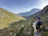 A smiling hiker standing on a rocky mountain trail with lush green valleys in the background.