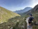 A smiling hiker standing on a rocky mountain trail with lush green valleys in the background.