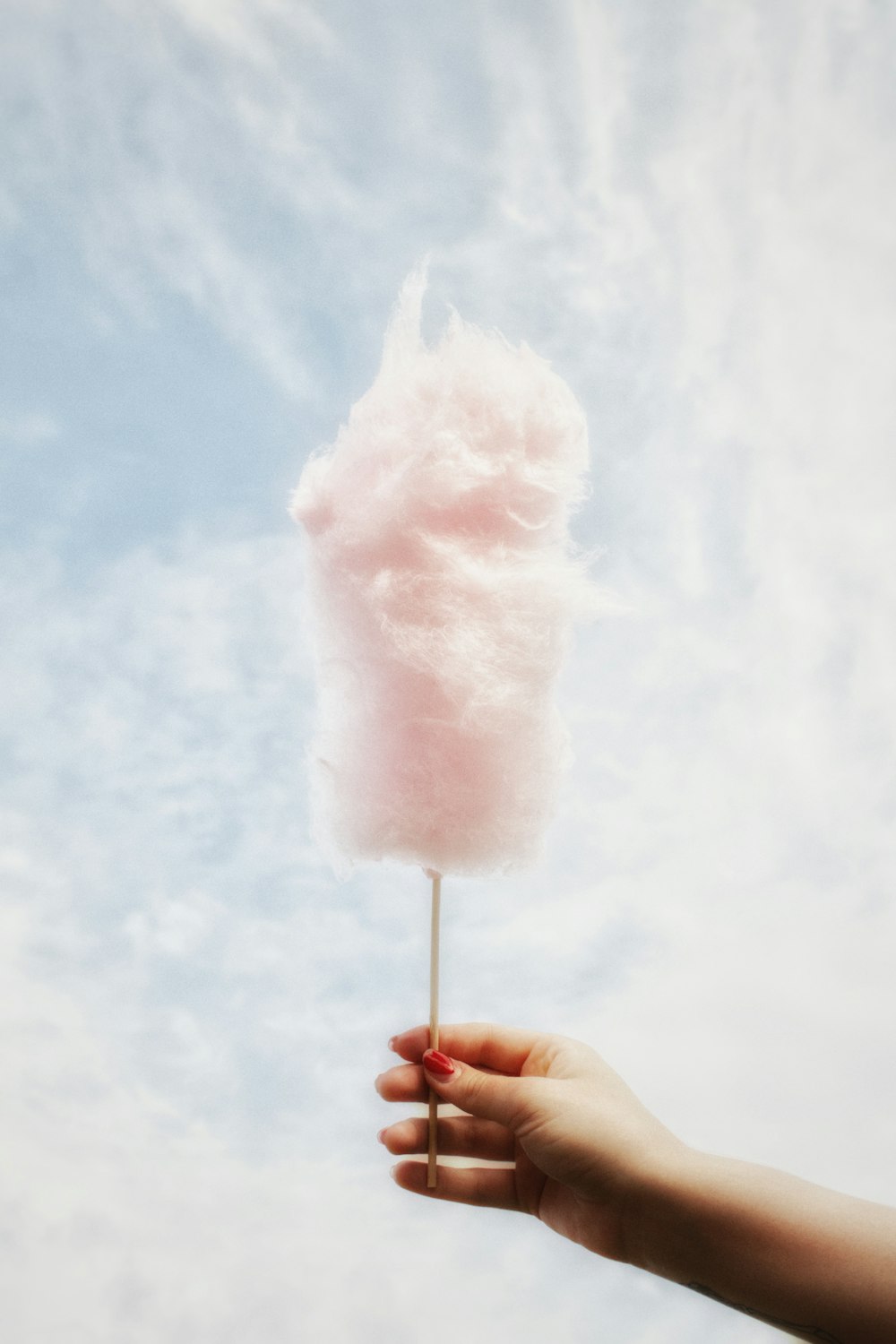 a hand holding a pink cotton candy on a stick
