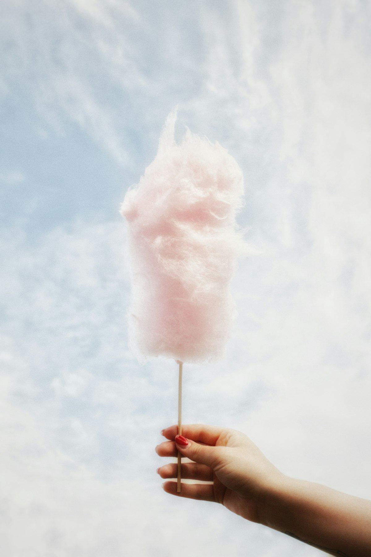 A hand holding a fluffy pink cotton candy stick &mdash; just like Trader Joe's new Sour Cherry Cotton Candy, one of this summer's most fun seasonal snack finds