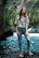 Happy woman posing near a scenic river during a tour with mountains in the background.