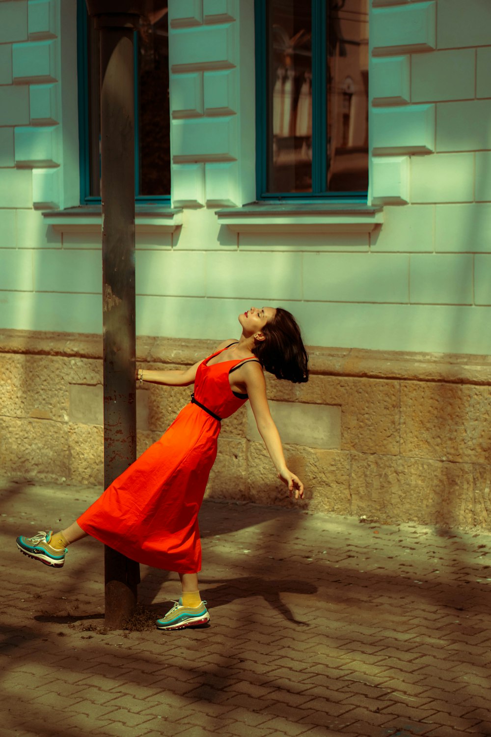 a woman in a red dress leaning against a pole