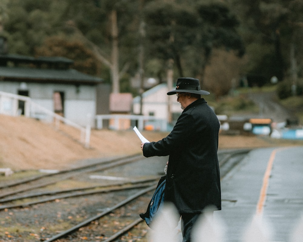 a man in a hat and coat walking down a train track