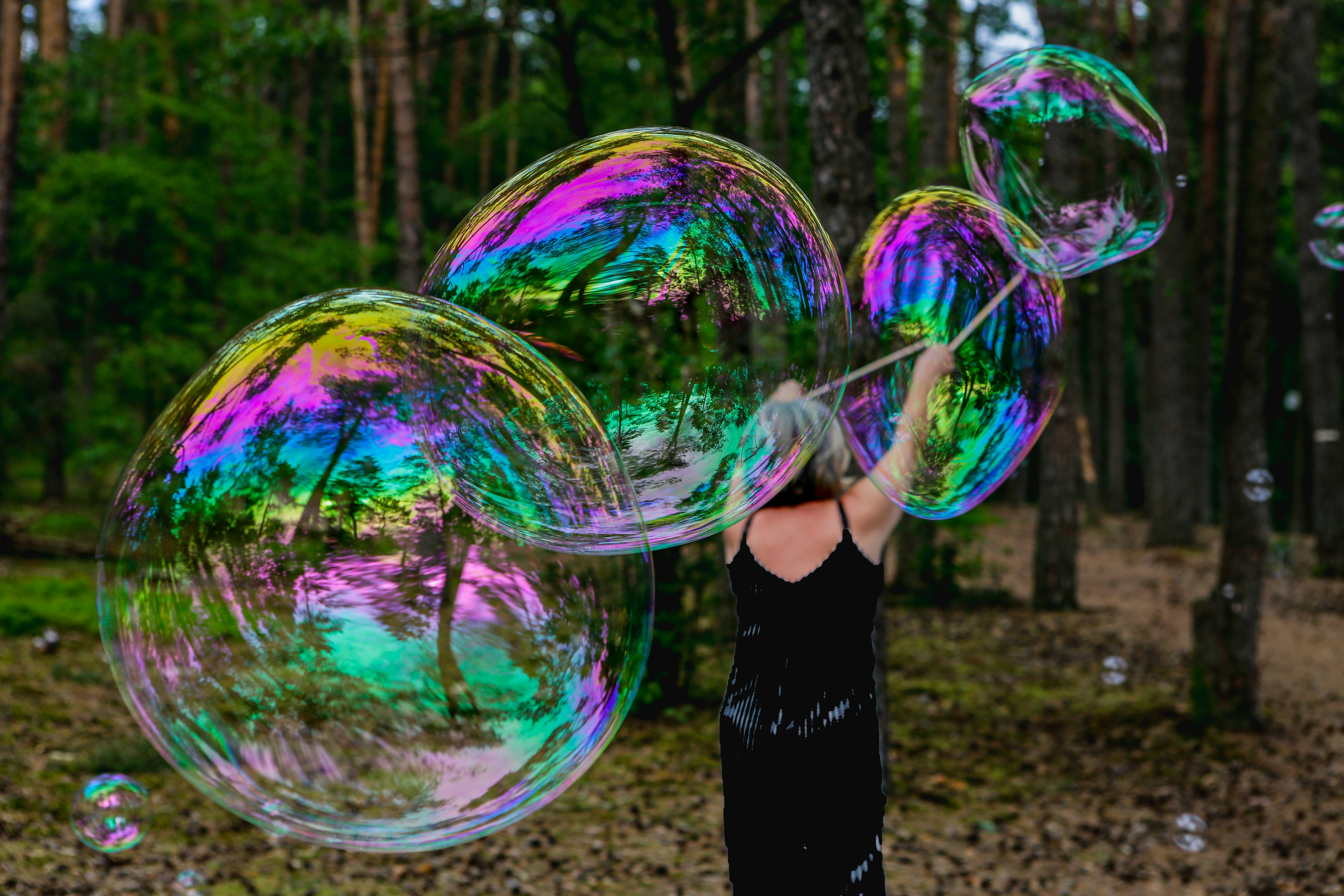 a woman in a black dress is holding three soap bubbles