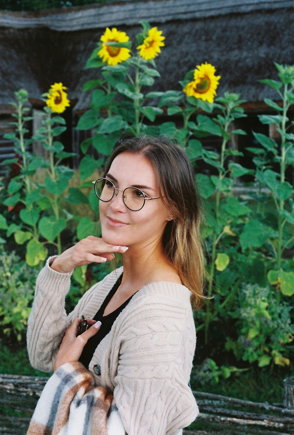 a woman wearing glasses standing in front of a field of sunflowers