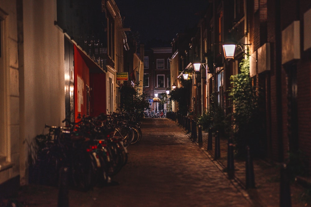 a narrow street at night with bicycles parked on the sidewalk