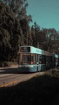 A sleek tram moving along a tree-lined urban street on a sunny day.