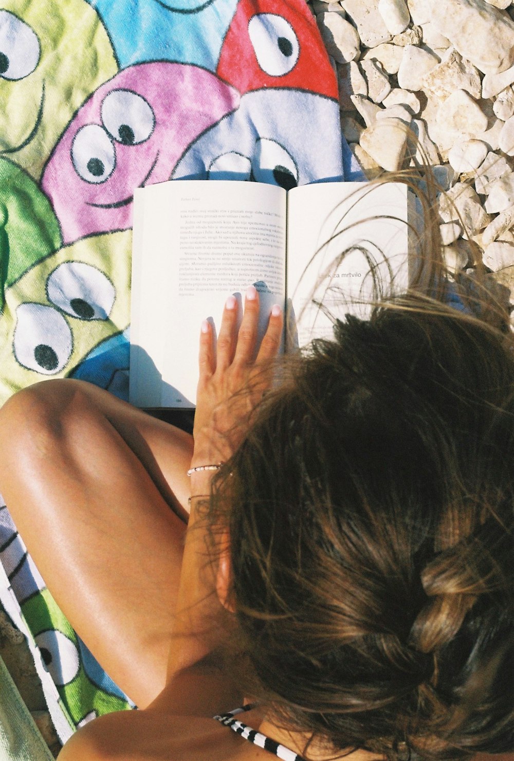 uma mulher lendo um livro em uma toalha de praia