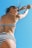 A person wearing a black and white striped bikini is captured from a low angle against a clear blue sky. The posture suggests movement, with arms raised and hair flowing slightly in the wind. Sunglasses add a stylish touch to the scene.
