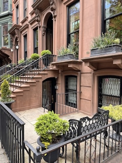 A charming brownstone townhouse with a classic New York City stoop and lush greenery.