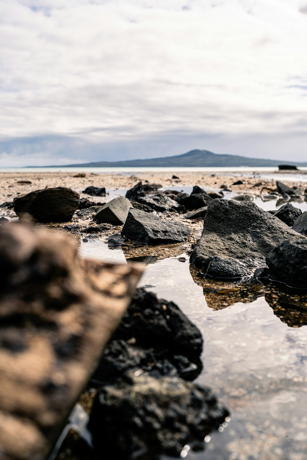 Rochas e água em uma praia com uma montanha ao fundo