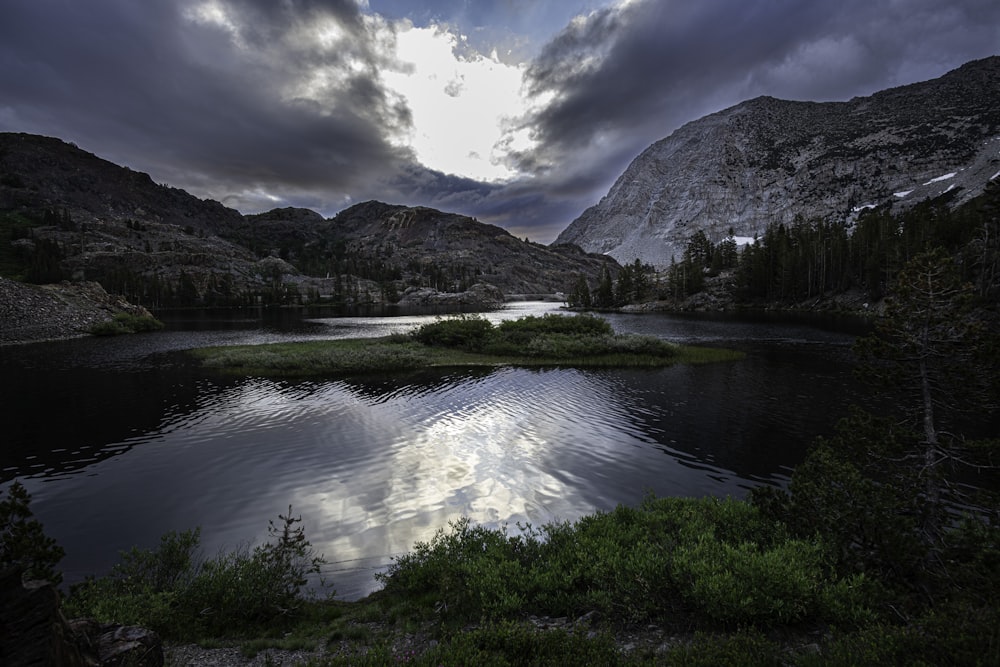 a lake surrounded by mountains under a cloudy sky